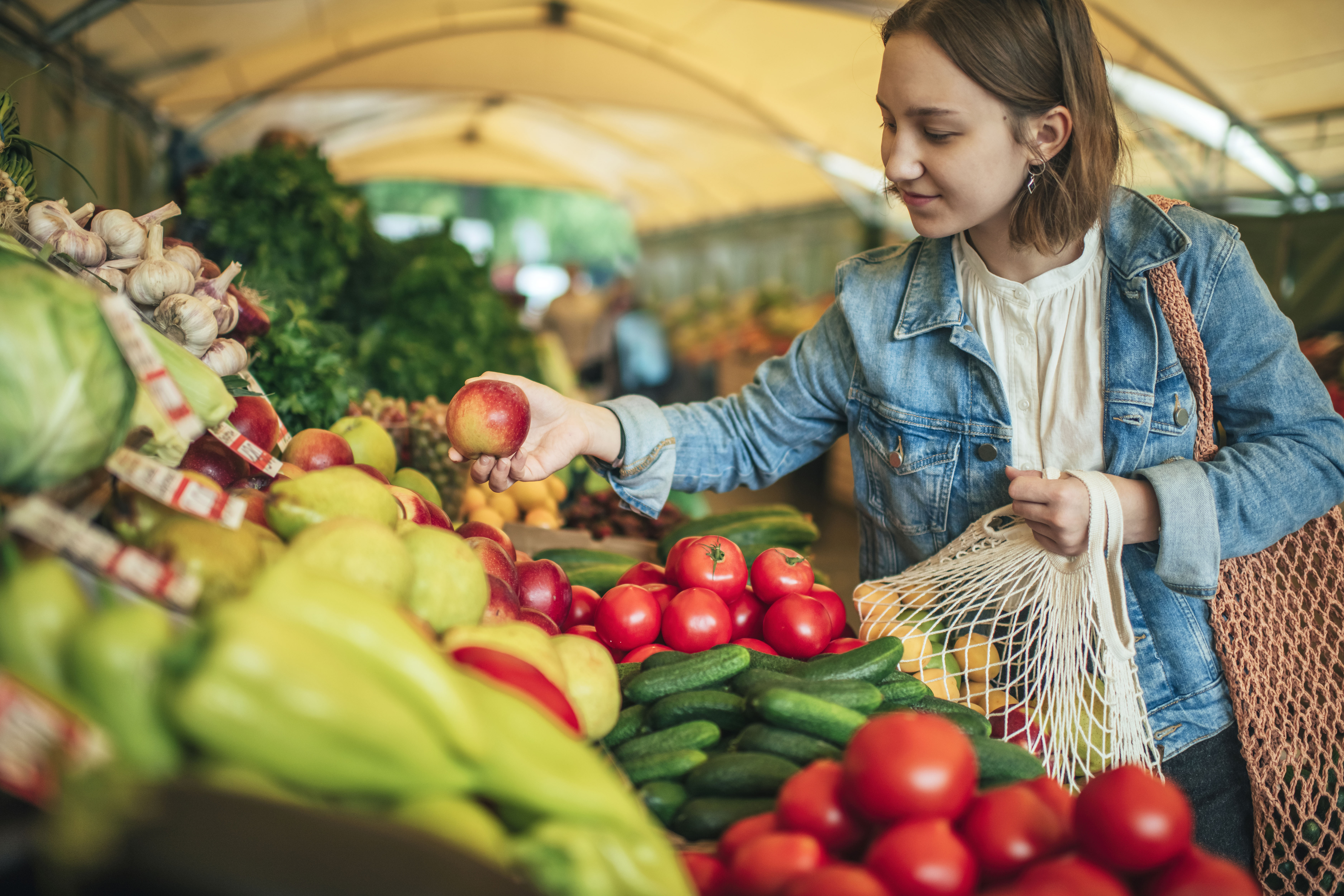 Woman shopping for apples at a covered farmers market booth.