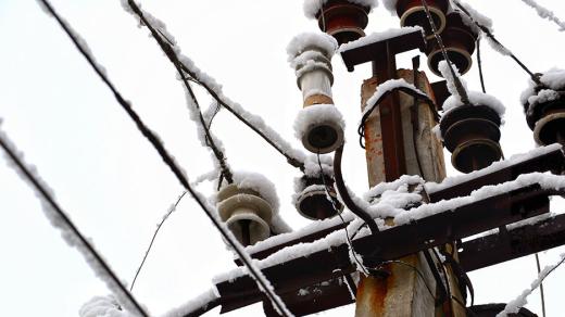 The top of an electrical pole and wires covered in snow.