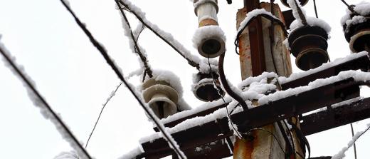 The top of an electrical pole and wires covered in snow.
