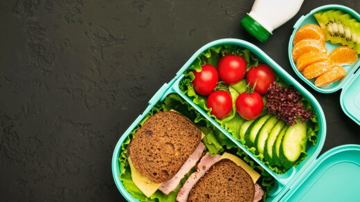 Packed school lunch of ham sandwich, fruit, and yogurt.
