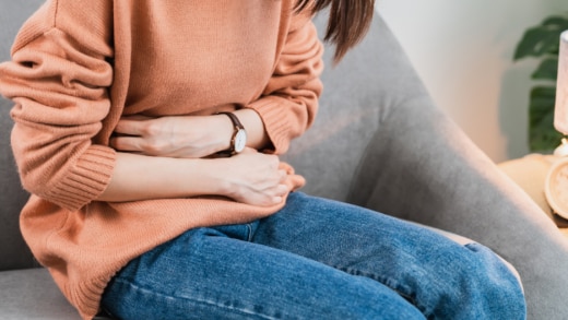 Person sitting hunched over, holding their stomach in discomfort.